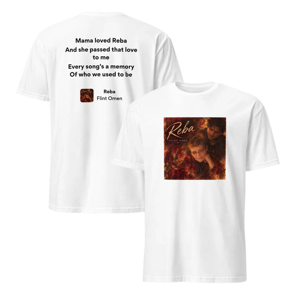 White Reba lyric T-shirt shown front and back. The front prints the Reba cover art: a woman in glasses and a young man among autumn-red leaves under the script title. The back reads “Mama loved Reba / And she passed that love to me” above a small cover badge.